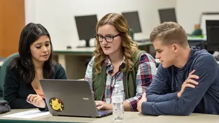 Students collaborating at a table viewing a laptop.