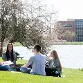 Fourstudentsreadingwhilesittingongrassbylake