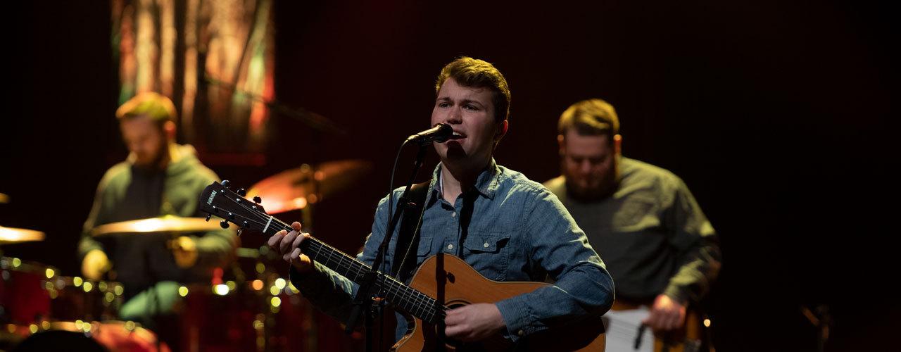 Student singing and playing guitar on stage